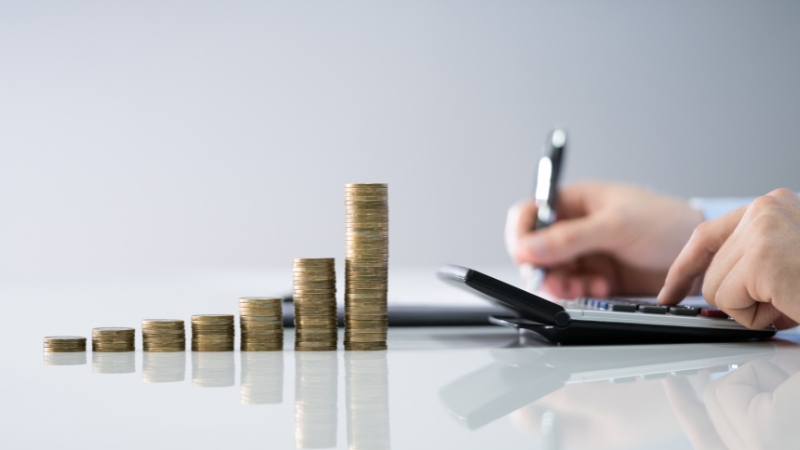 Osoba računa troškove na kalkulatoru pored složenih kovanica koje rastu