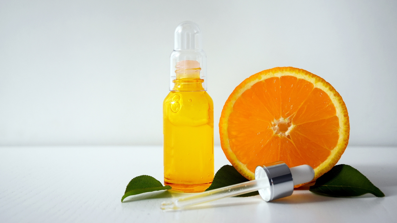 Serum sa vitaminom C stoji pored kriške pomorandže i pipete na beloj podlozi